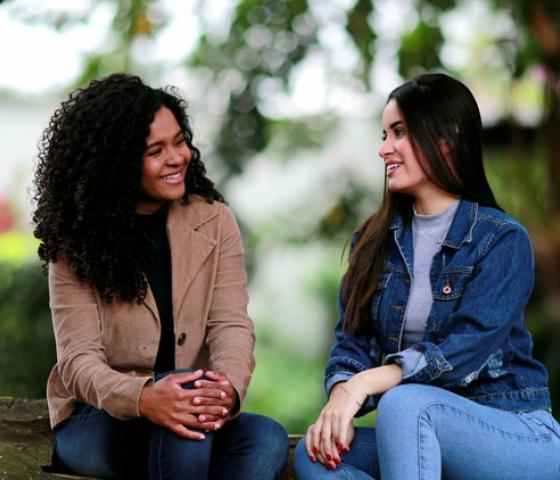 Two women sitting on a bench in a park setting talking