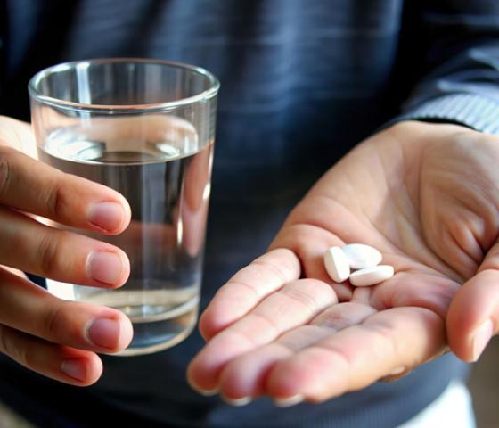 hand with tablets and other hand with glass of water